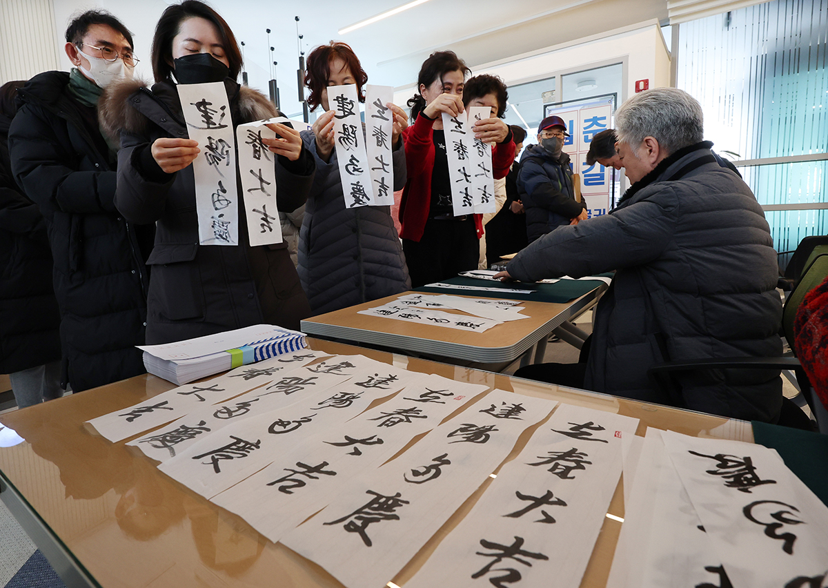 A calligrapher on Jan. 16 hands out free ipchunbang, or written messages posted on the day of Ipchun, the traditional start of spring based on the 24 solar terms of the country's lunar calendar, that he wrote at an ipchunbang sharing event hosted by Daedonggol Cultural Center in Busan's Nam-gu District. 